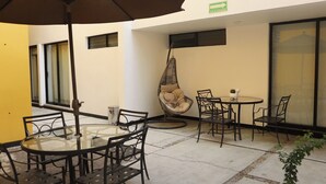 A patio area with a round glass table, black metal chairs, a hanging chair, and a large umbrella. - Hotel Casa Kabii (Oaxaca)