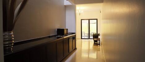 A hallway with a kitchen area on the left, a dining area with a table and chairs, and a view of the outdoors through a glass door.