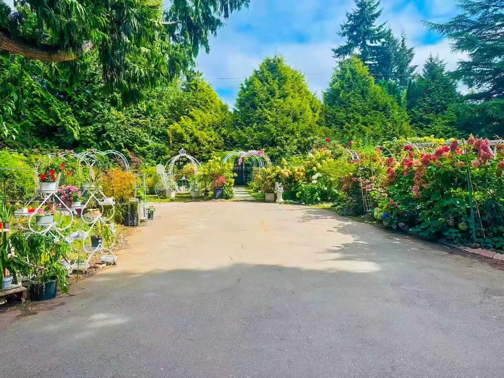 Une allée pavée mène à un jardin où l’on trouve différentes sortes de plantes et de fleurs.