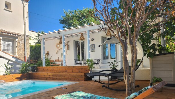 Eine Holzterrasse mit Pool, Liegestühlen und einer Pergola mit Gartenmöbeln.