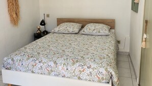 Ein ordentlich bezogenes Bett mit Blumenmuster, eine Nachttischlampe und eine Wandleuchte.