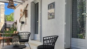 Ein überdachter Patio-Bereich mit zwei schwarzen Metallstühlen, einem kleinen Tisch und einem dekorativen gewebten Korb.