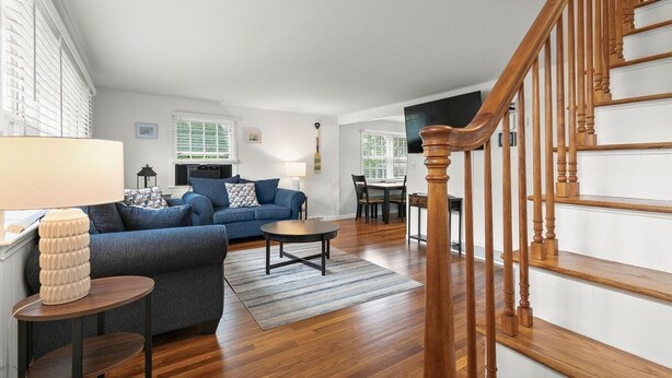A spacious living room with a blue sofa, a wooden staircase, and a dining area. - Modern Falmouth Home Close to Water and Town (Falmouth)