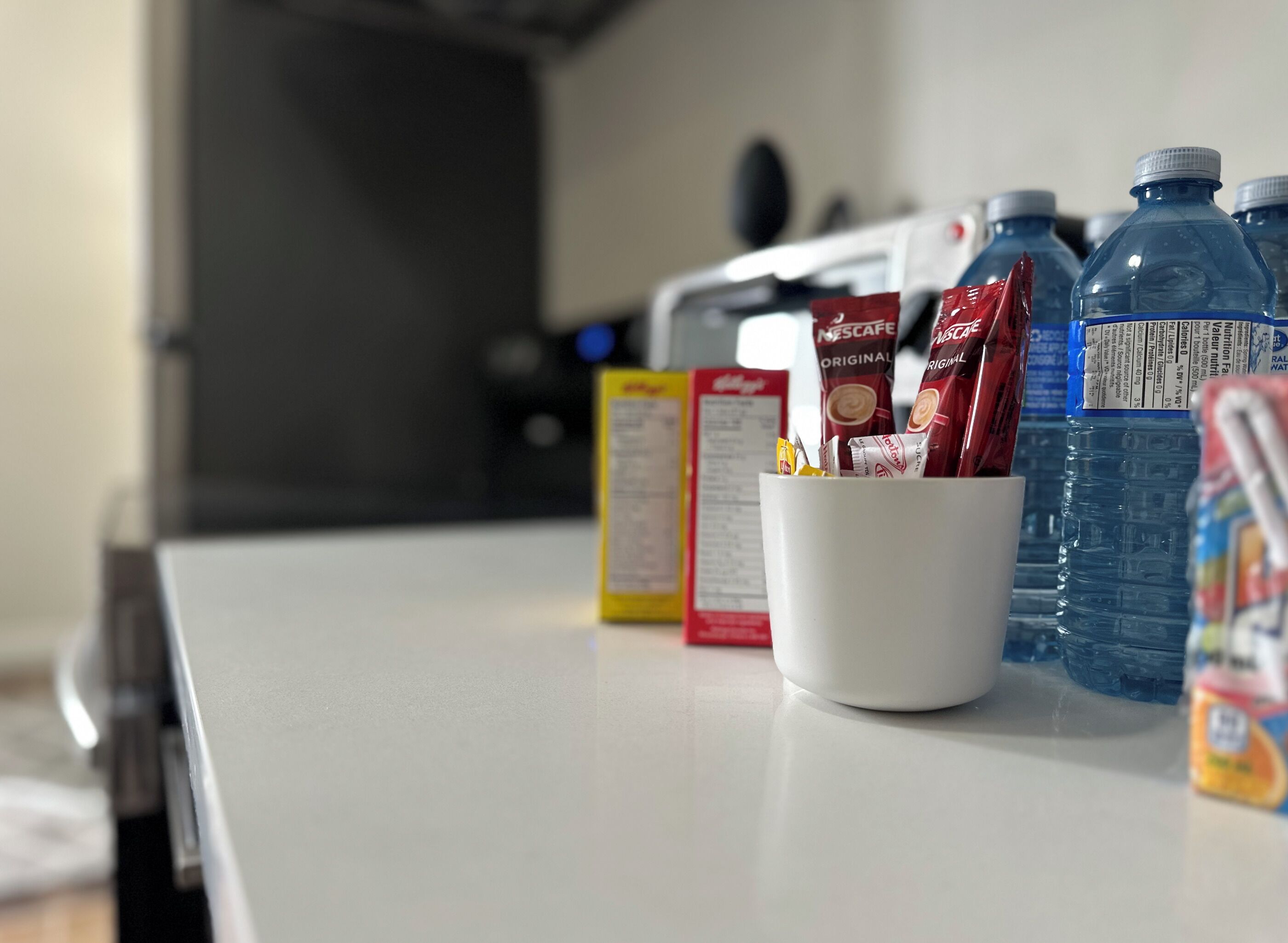 A kitchen counter with a white mug containing coffee pods, a water bottle, and a carton of milk.
