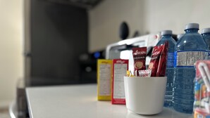 A kitchen counter with a white mug containing coffee pods, a water bottle, and a carton of milk.