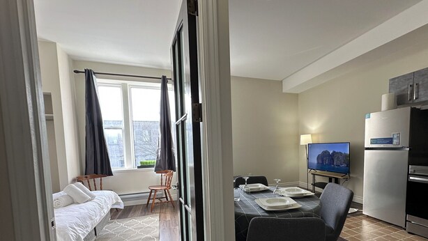 A hotel room with a bed, a dining table with chairs, a TV, and a refrigerator.