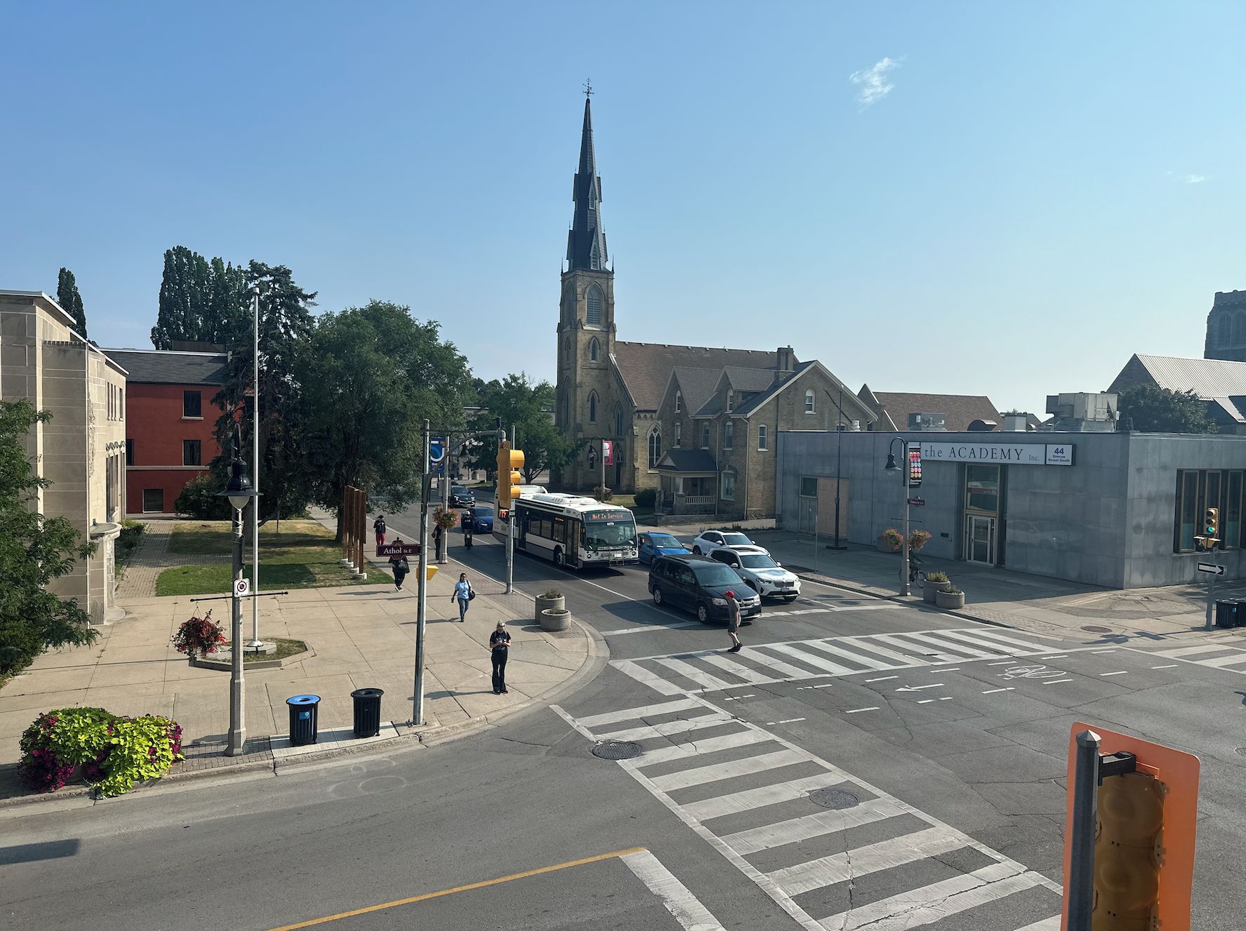 Una intersección de calles con una aguja de iglesia, una parada de autobús y un edificio con la leyenda 'The Academy Inc.'