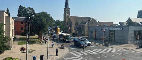 Una intersección de calles con una aguja de iglesia, una parada de autobús y un edificio con la leyenda 'The Academy Inc.'