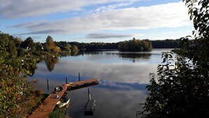 Een kalm meer met een houten steiger die in het water reikt, omgeven door bomen en een heldere lucht.