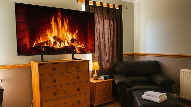 Una habitación acogedora con chimenea, un sofá de cuero, un aparador de madera y un televisor mostrando fuego.