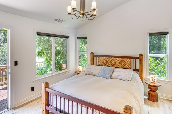 A bedroom with a large bed, two windows, a chandelier, and a wooden headboard. - 1 Mi to Lake Gregory! Forest-View Crestline Cabin (Crestline)