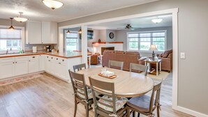 A spacious kitchen with white cabinets, a dining table with chairs, and a living area with a sofa and a coffee table. - Bring Your Boat! Little Traverse Lake Getaway (Maple City)