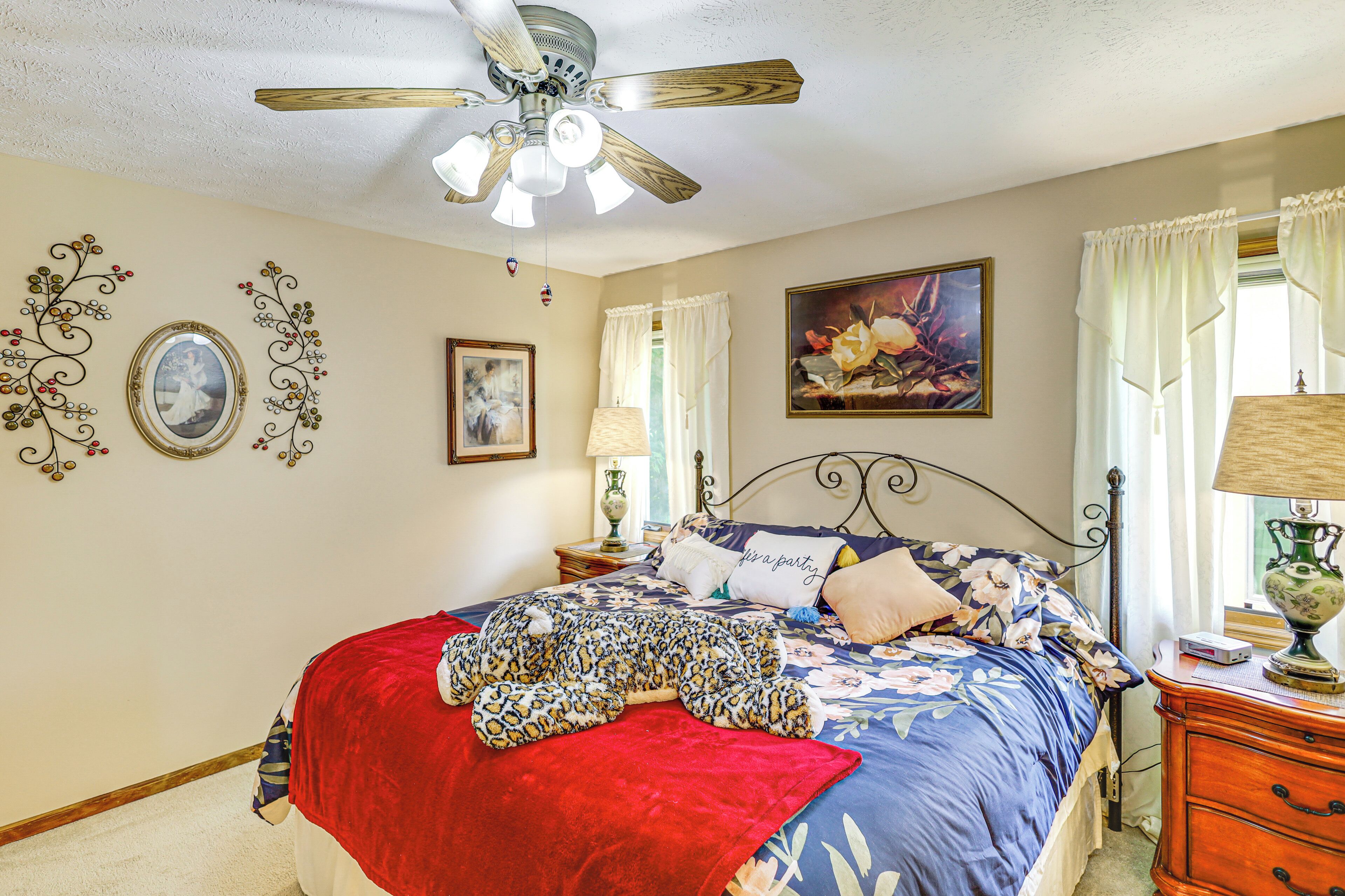 A bedroom with a bed, a ceiling fan, decorative wall art, and a nightstand with a lamp.