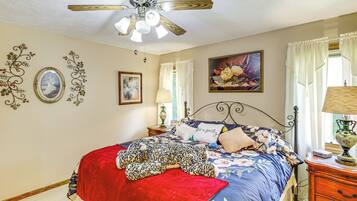 A bedroom with a bed, a ceiling fan, decorative wall art, and a nightstand with a lamp.