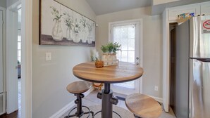 A kitchen with a round wooden table, two stools, a refrigerator, and a painting of vases on the wall. - 1 Mi to Tulsa Arts District: Home w/ Yard! (Tulsa)