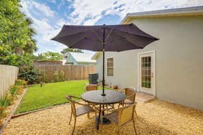 Une terrasse avec une table et des chaises, un parasol et un petit coin jardin.