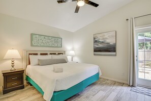 Une chambre à coucher avec un lit, des tables de chevet, un ventilateur de plafond, des œuvres d’art et une vue sur l’extérieur, visible à travers une porte.