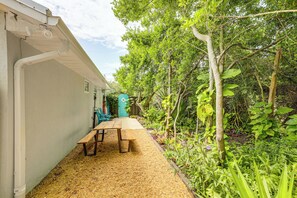 A garden with a wooden bench and a teal chair, surrounded by lush greenery and trees.