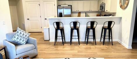 A modern kitchen with white cabinets, a central island with bar stools, and a dining area with a sofa and coffee table.