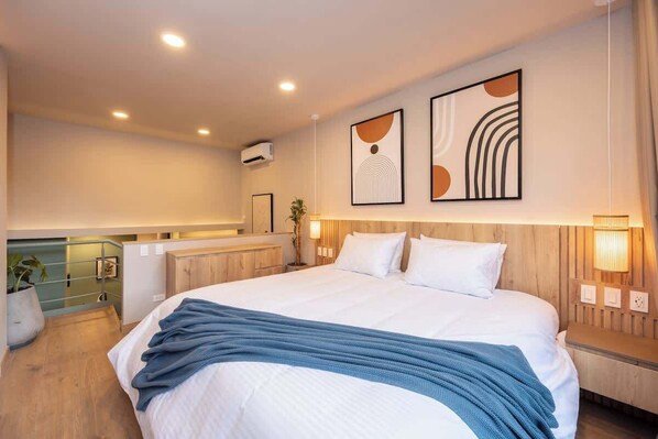 A modern hotel room with a large bed, a wooden headboard, and abstract wall art.