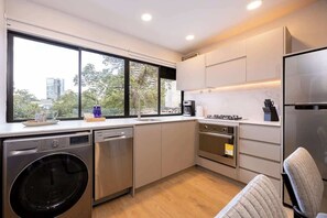 A modern kitchen with stainless steel appliances, a dishwasher, and a large window offering a city view.
