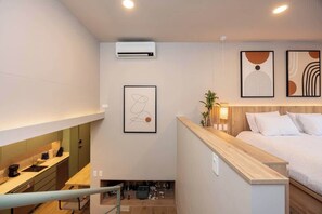 A modern hotel room with a kitchenette, a bed with white bedding, and artwork on the walls.