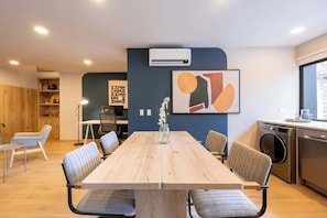 A modern meeting room with a long wooden table, comfortable chairs, a whiteboard, and an air conditioning unit.