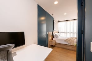 A modern bedroom with a bed, bedside table, lamp, and a TV on a desk. - Digital Nomad Paradise 2 units-4BR w/ AC in Manila (Medellín)