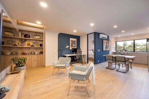Un espacio habitable moderno y abierto con cocina, comedor y zona de estar. Hay estanterías empotradas con objetos decorativos y un gran ventanal que proporciona luz natural.