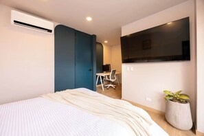A bedroom with a bed, a desk, a chair, a potted plant, and a TV mounted on the wall.