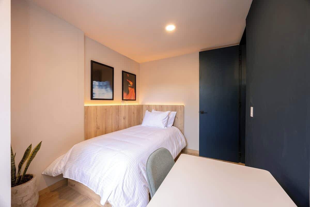 Quarto moderno com cama, mesa de cabeceira, planta em vaso e duas imagens emolduradas na parede.