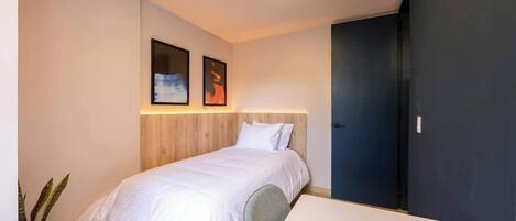 A modern bedroom with a bed, a bedside table, a potted plant, and two framed pictures on the wall.