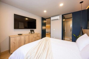 A modern bedroom with a large bed, a wooden dresser, a mirror, and an air conditioning unit.