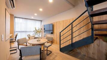 Una sala de estar moderna con una mesa redonda, sillas, un televisor montado en la pared y una escalera de madera.