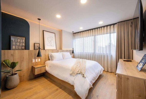 Un dormitorio moderno con una cama grande, mesitas de noche, una planta en maceta y un televisor.