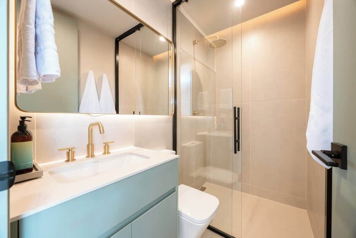 A modern bathroom with a glass-enclosed shower, a white sink with gold fixtures, and a large mirror.