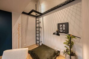 A compact room with a loft bed, a ladder, a small desk, and a potted plant.
