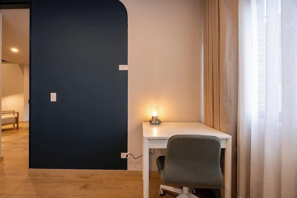 A room with a desk, chair, and a lamp. There is a door with a light switch and a power outlet.