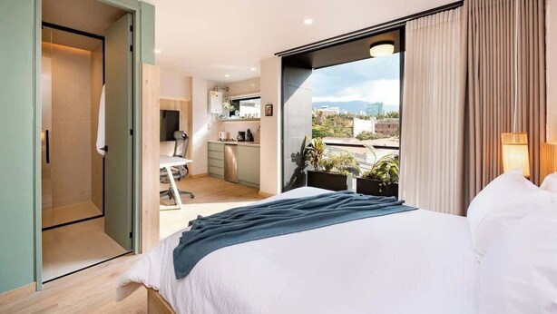 A modern hotel room with a large bed, a kitchenette, and a balcony with a city view. - Digital Nomad Paradise 3 units-4BR w/ AC in Manila (Medellín)