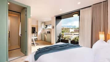 Quarto de hotel moderno com uma cama grande, uma kitchenette e uma varanda com vista para a cidade.