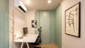 A small office with a white desk, a computer, a chair, an air conditioner, and a framed abstract painting on the wall. - Digital Nomad Paradise 3 units-4BR w/ AC in Manila (Medellín)
