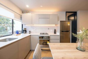 A modern kitchen with a built-in oven, a refrigerator, and a dining area with a wooden table and chairs. - Digital Nomad Paradise 3 units-4BR w/ AC in Manila (Medellín)