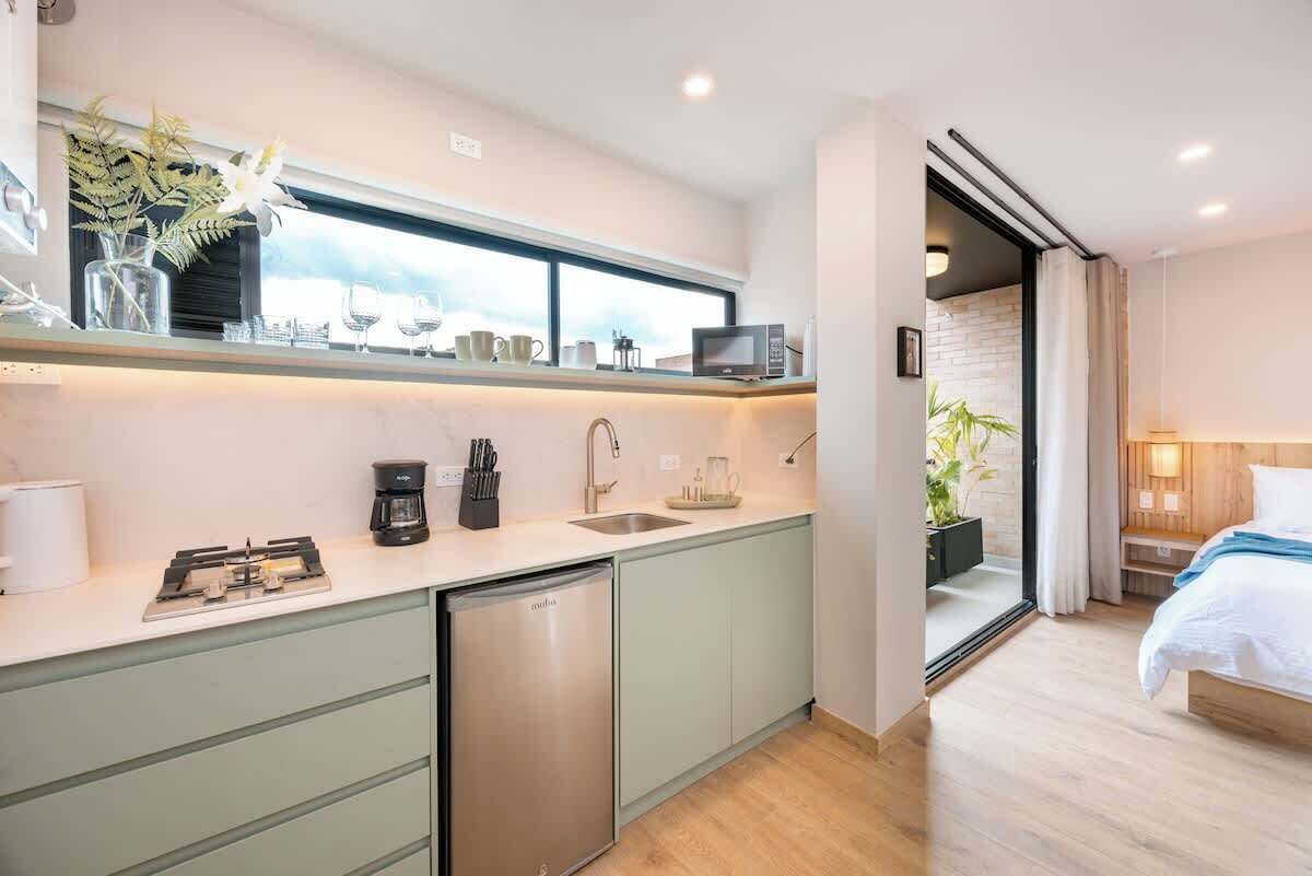 Cocina compacta equipada con lavavajillas, cafetera y microondas. Hay una ventana sobre el fregadero y una planta en el alféizar.
