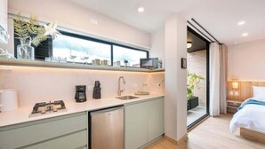 A compact kitchen with a dishwasher, a coffee maker, and a microwave. There is a window above the sink and a plant on the windowsill. - Digital Nomad Paradise 3 units-4BR w/ AC in Manila (Medellín)