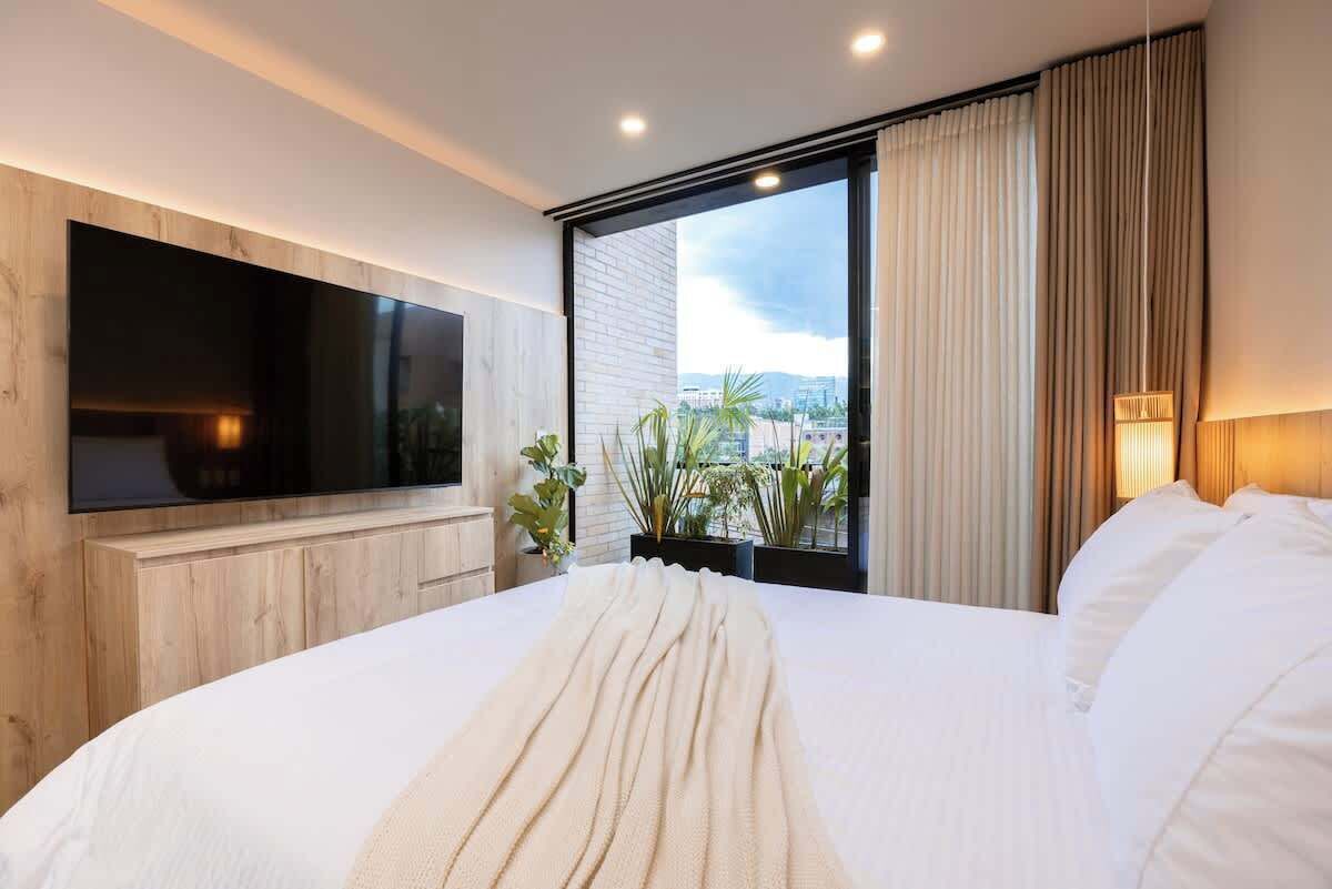 Une chambre d’hôtel moderne dotée d’un grand lit, d’un téléviseur à écran plat fixé au mur et d’une grande fenêtre donnant sur la ville.