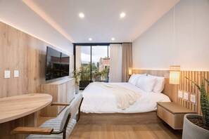 Ein modernes Hotelzimmer mit einem großen Bett, einem an der Wand montierten Fernseher, einem Esstisch und einer Zimmerpflanze.