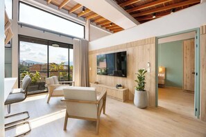 Ein modernes Wohnzimmer mit großem Fernseher, Holzboden und Balkon mit Pflanzen.