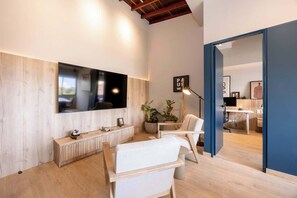 A modern living room with a large flat-screen TV mounted on the wall, a wooden console table, a white sofa, and a floor lamp.