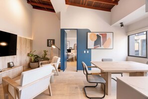 Un espace de bureau moderne avec un banc en bois, un bureau et une grande table. On y trouve des plantes en pot et un tableau accroché au mur.