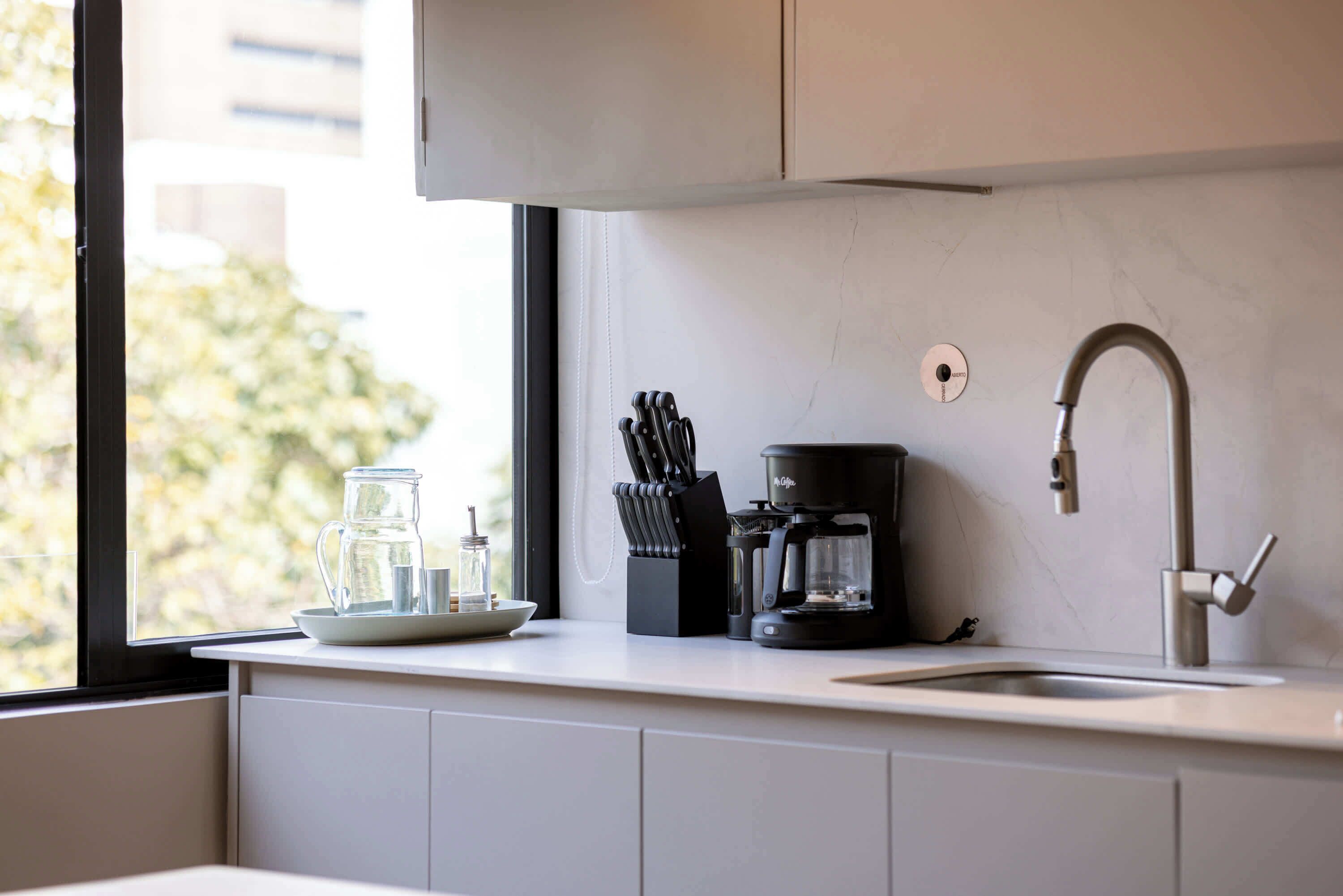 Uma cozinha moderna com cafeteira, conjunto de facas e jarra sobre o balcão.